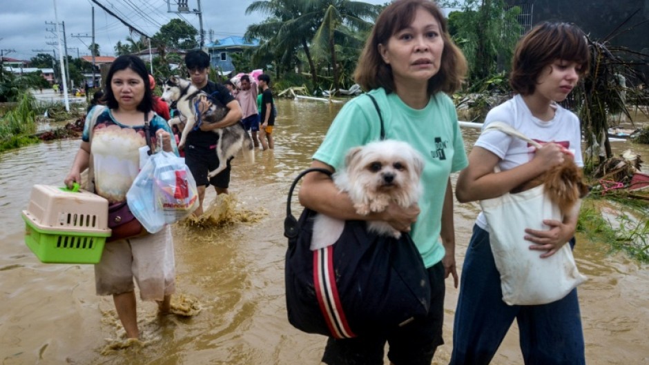 Residents carrying their belongings and pet dogs wade through a flooded street as they evacuate from their inundated homes in Liloan town, Cebu province