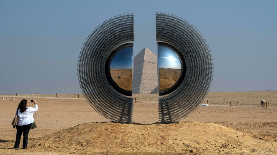 A woman takes a picture of the art installation "The Shen" by artist by Mert Ege Kose during the fifth edition of the "Forever is Now" art exhibition by Art d’Egypte at the Giza pyramids necropolis