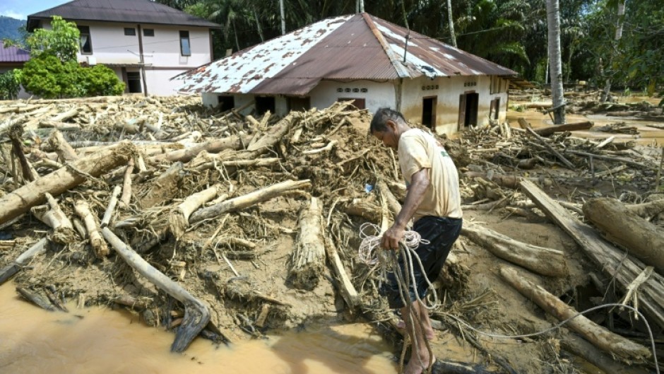 A villager walks among a pile of logs in flood-hit Tukka village in Indonesia