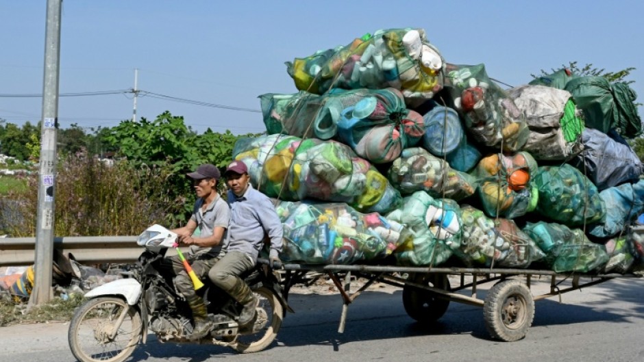 Men on a motorbike pull a cart carrying plastic waste on the outskirts of Hanoi