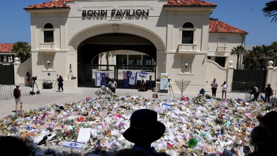 Mourners stand near tributes piled together at the front of the Bondi Pavilion, in memory of the victims of the Bondi Beach shooting