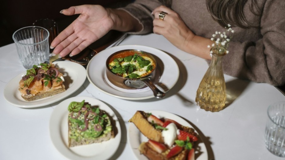 A patron poses at a table with an array of half-sized portions of meals that some restaurants are offering as more and more people have smaller appetites due to weight-loss drugs like Ozempic