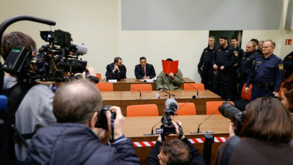 The defendant, partially identified as Farhad N., hides his face behind a folder at the start of his trial in Munich
