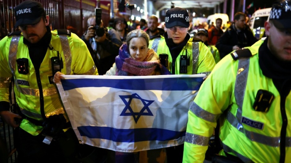 Police officers escort a woman with an Israeli flag away from Pro-Palestinian protesters outside Villa Park in Birmingham on November 6, 2025 ahead of the UEFA Europa League league-stage football match between Aston Villa and Maccabi Tel Aviv