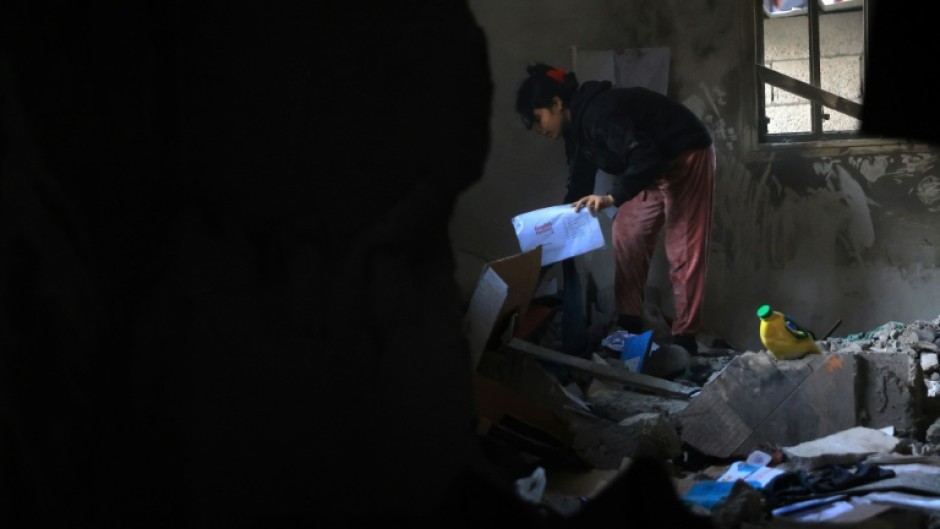 A Palestinian girl picks up her school work from the debris of a destroyed house