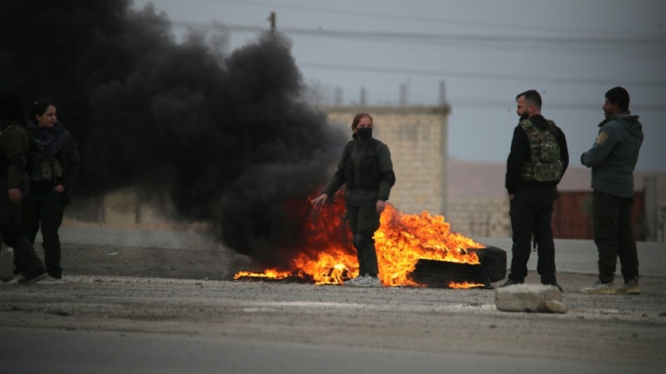 Kurdish fighters stand near burning tires at the entrance to the city of Tabqa in the northern Syrian Raqa province, on January 17, 2026
