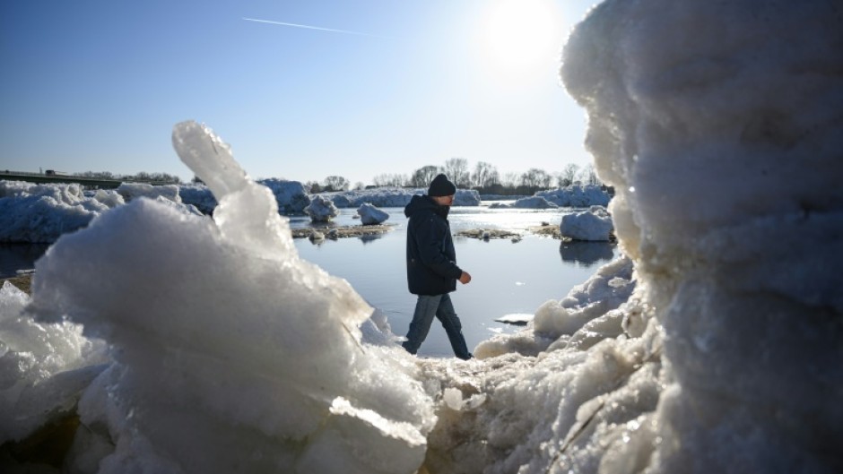 A passerby walks past large chunks of ice washed up along the banks of the Elbe river near Geesthacht, northern Germany, on January 19, 2026.