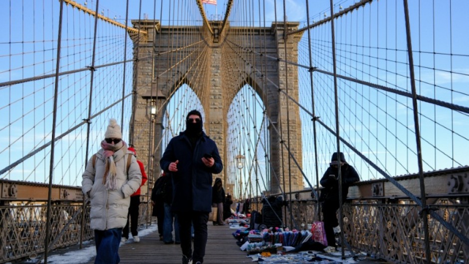 People brave the cold temperatures while walking on the Brooklyn Bridge in the Manhattan borough of New York City on January 21, 2026