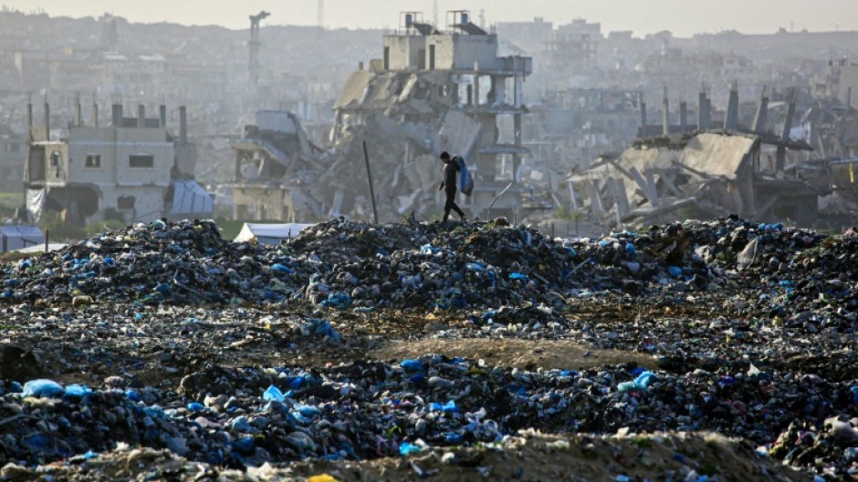 A Palestinian boy searches for recyclable material at a landfill against the backdrop of destroyed buildings in Khan Yunis, in the southern Gaza Strip
