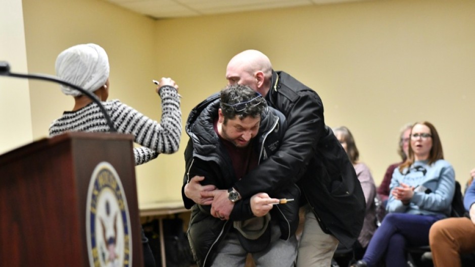 Security restrains a man who sprayed an unknown substance at US Representative Ilhan Omar (D-MN) (L) during a town hall she was hosting in Minneapolis