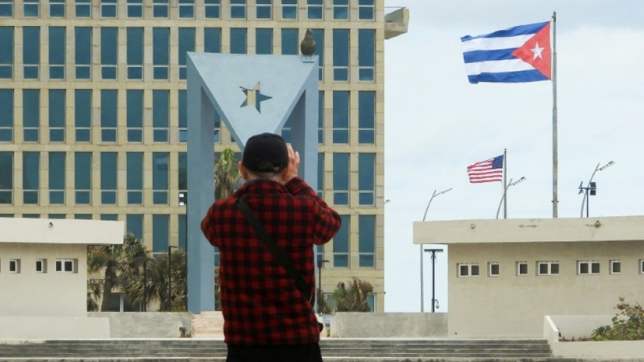 A tourist takes pictures of the US Embassy with the US flag and the Cuban flag in the background in Havana