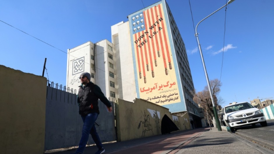 A man walks past a large anti-US mural on the side of a Tehran building