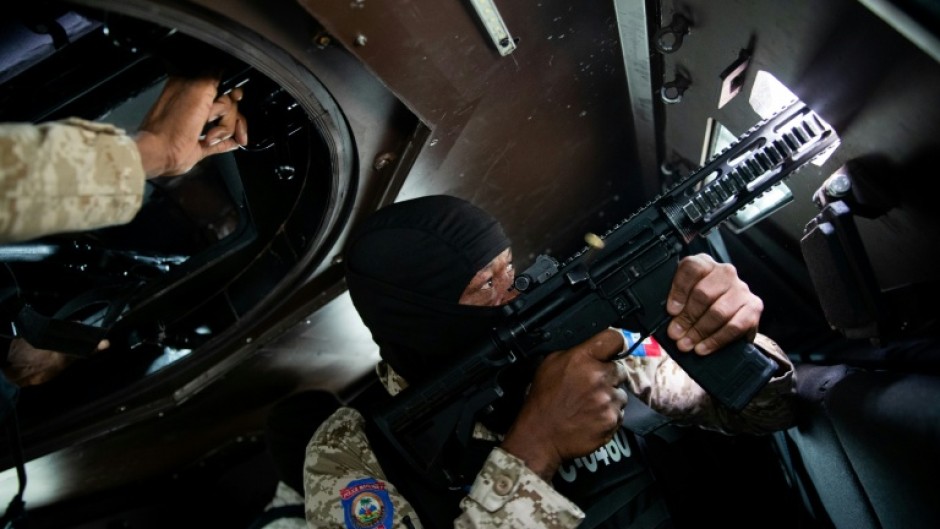 A Haitian police officer aims his weapon out a window of an armored vehicle during a patrol in downtown Port-au-Prince in January 2026
