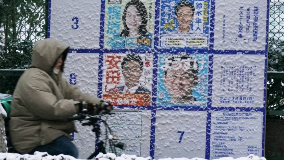 A person rides past a board displaying posters of candidates for the Lower House election on February 8, 2026