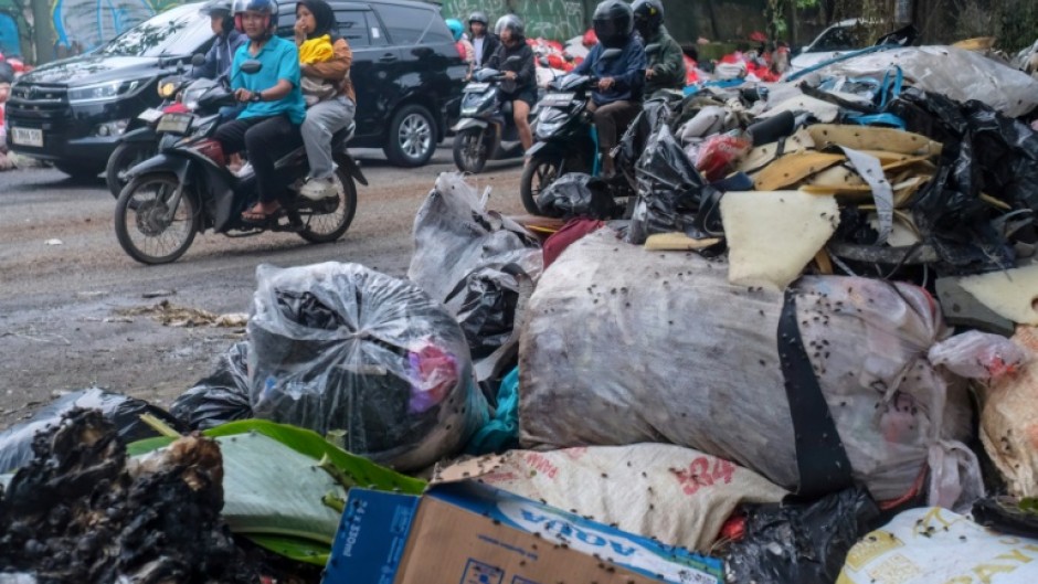 Vehicles driving along a road littered with illegally dumped waste in Pamulang, South Tangerang, Banten