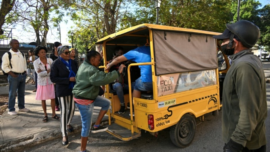 People line up to board an electric tricycle on a street in Havana