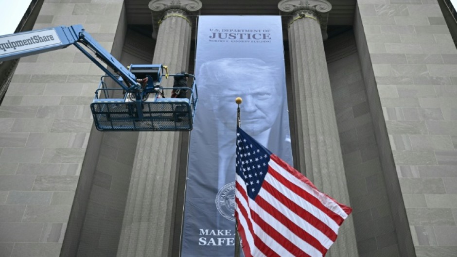 Workers on an aerial lift watch after installing a new banner featuring an image of US President Donald Trump on the facade of the US Department of Justice headquarters building in Washington, DC