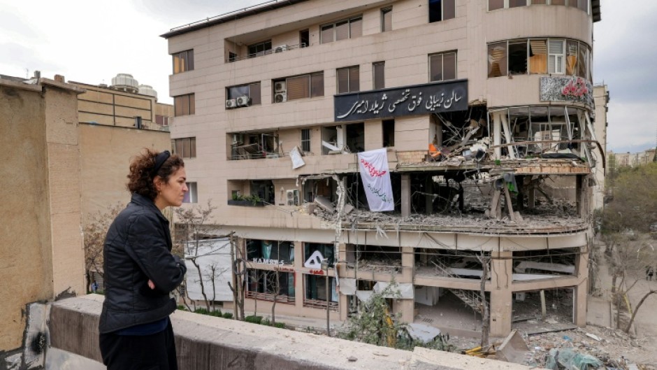 A woman standing on a rooftop in Tehran views destruction in an office building that housed the offices of the Doha-headquartered news network Al Araby TV following a missile strike on March 29, 2026