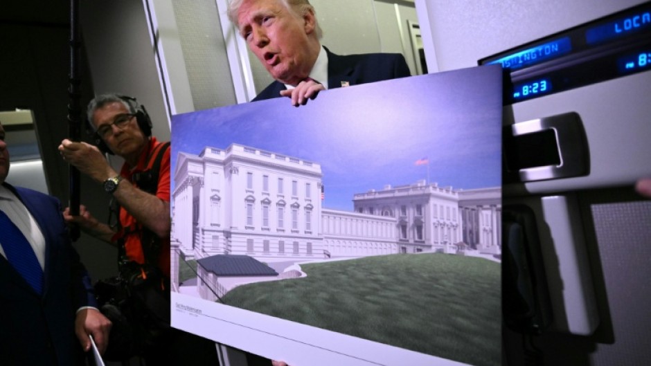 US President Donald Trump holds a rendering of the East Wing modernization as he speaks to reporters aboard Air Force One