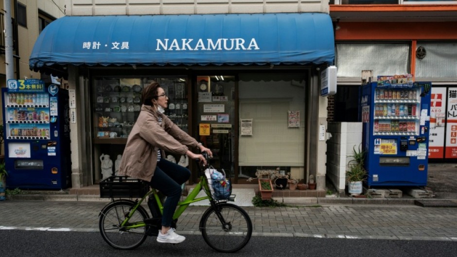 A woman cycles past two vending machines next to a clock shop in Tokyo's Bunkyo district on April 14, 2026