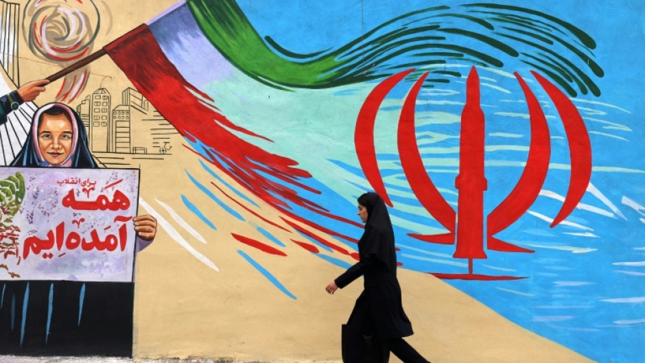 An Iranian woman walks past an anti-US and anti-Israel mural in Tehran