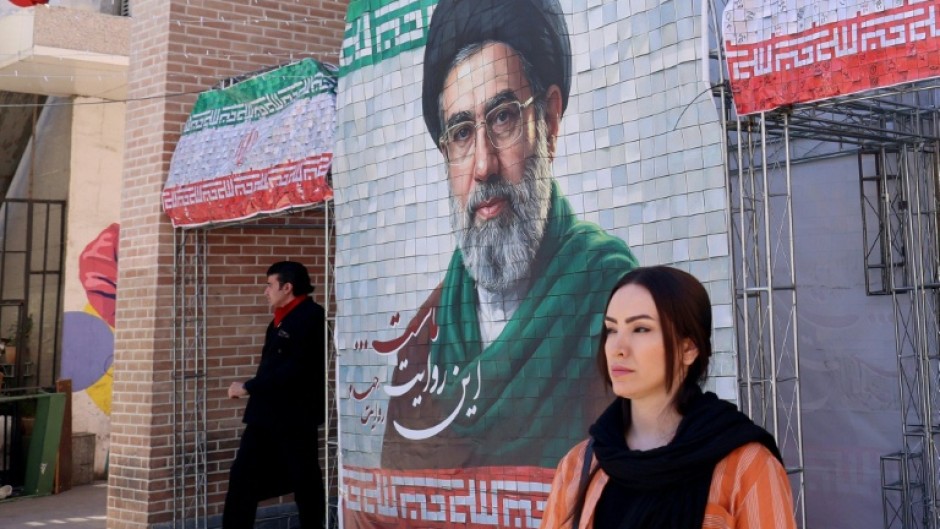 A woman walks past a large tiled image of Iran's current leader Ayatollah Mojtaba Khamenei outside a metro station in Tehran
