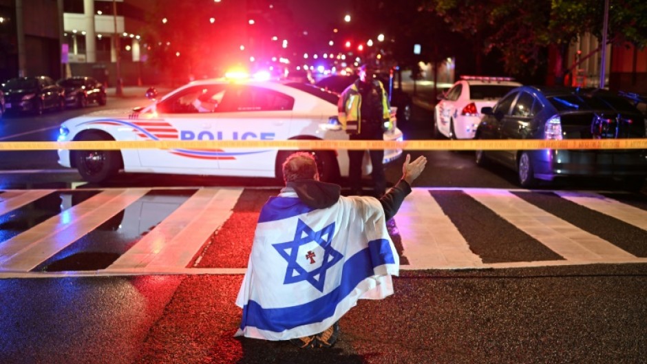 A man draped in the Israeli flag, bearing a cross and the name 'Jesus' at its center, gestures as Metropolitan Police officers secure the area outside the Capital Jewish Museum