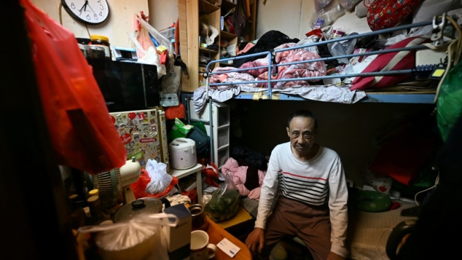 Guan Ci sits on his bed in his subdivided housing unit in Kowloon, Hong Kong