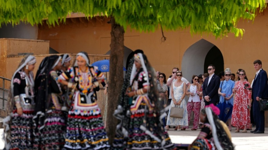 Artists wearing traditional attire and members of US Secretary of State Marco Rubio's team wait in the shade as he tours the Amber Fort in Jaipur