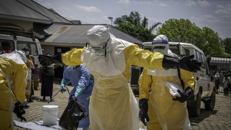 Health workers are doused with disinfectant after contact with the body of one presumed Ebola fatality