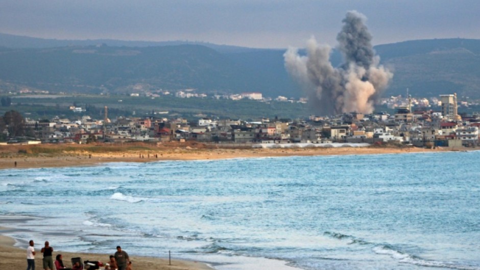 People visit beach against the backdrop of smoke rising from the site of an Israeli strike near the southern Lebanese city of Tyre on May 27