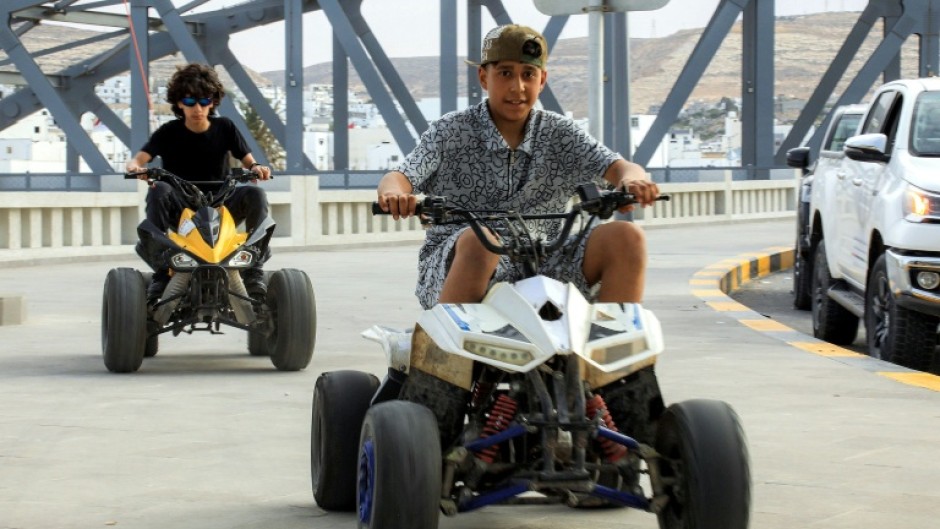 Children ride all-terrain vehicles (ATVs) along a pedestrian pavement in Derna