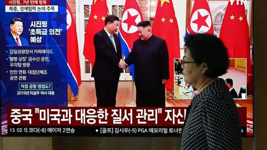 A woman walks past a television screen in Seoul Monday showing a news broadcast with file footage of the 2019 meeting between China's President Xi Jinping and North Korean leader Kim Jong Un