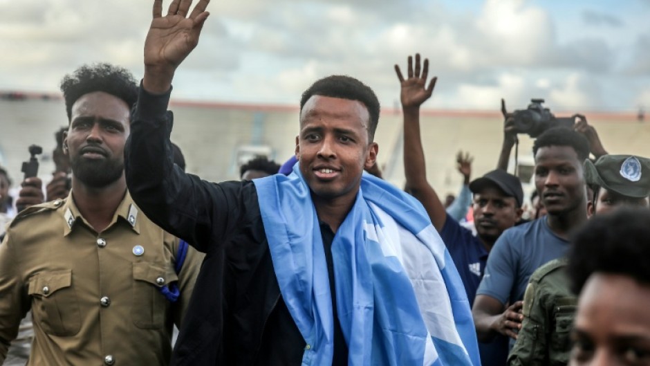 Somali referee Omar Artan waves to supporters while draped in the Somali flag as he is welcomed after returning to Mogadishu after being denied entry to the United States for the World Cup