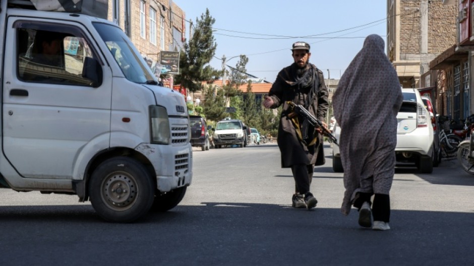 An Afghan burqa-clad woman walks past a Taliban security personnel standing guard outside a mosque in Shahrak-e-Almahdi, Jebrail district of Herat Province on June 11, 2026