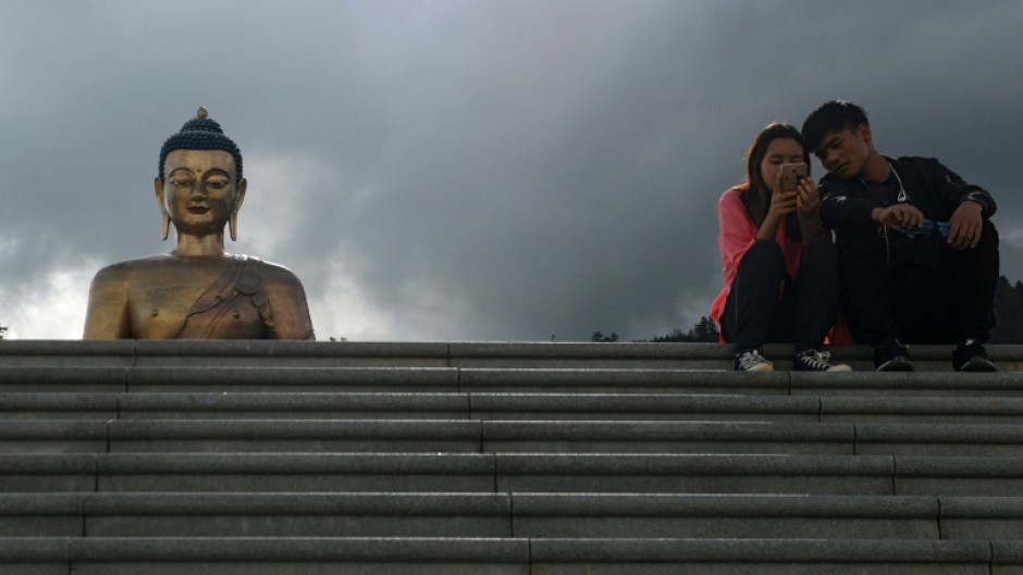 People look at a phone as they sit beside the Buddha Dordenma statue in Bhutan's capital Thimphu on August 25, 2018