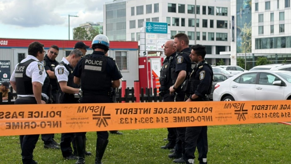 Damaged windows can be seen in the distance as police gather near the scene of a shooting in Montreal, which left three people dead