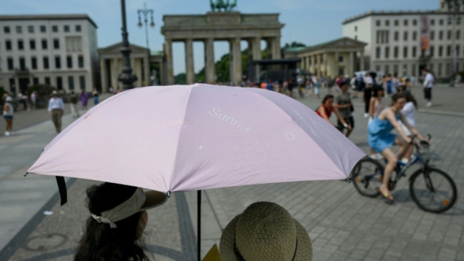 People shelter from the sun under umbrellas at Berlin's Brandenburg Gate