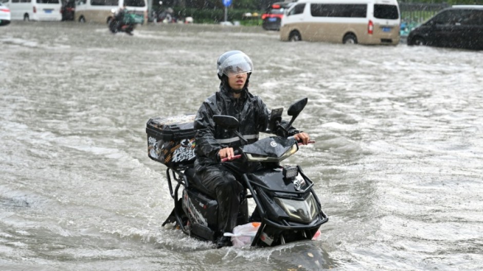A man on a scooter makes his way along a flooded street in Beijing