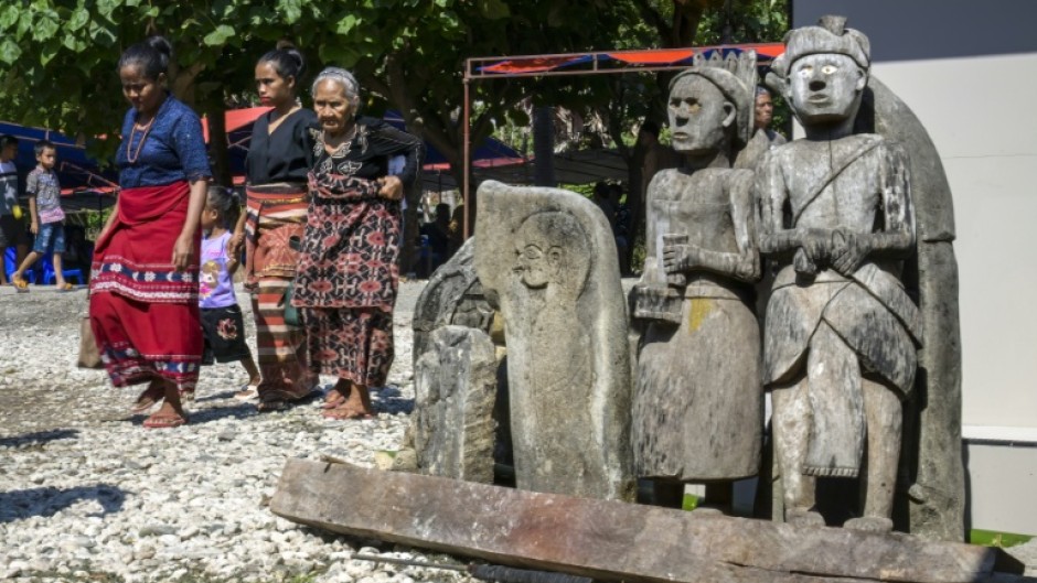 Sumbanese women wearing local ikat fabrics pass some of the statues and tombs that dot every village
