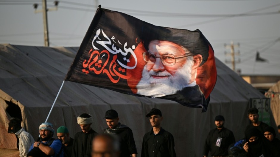 Shiite Muslim pilgrims hold a flag bearing the portrait of Iran's slain supreme leader Ayatollah Ali Khamenei as they march to the Iraqi city of Karbala
