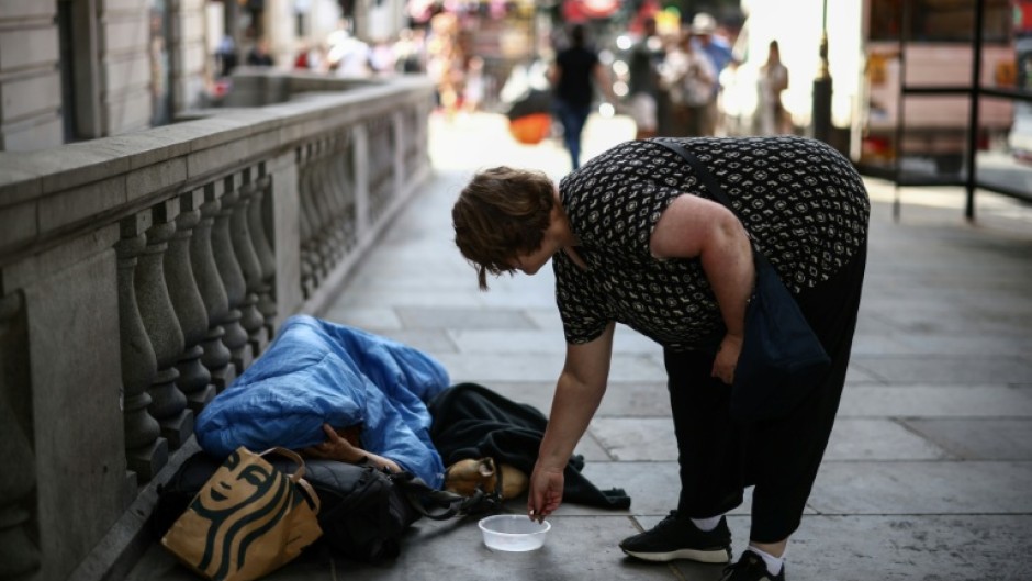 A woman puts some coins in a dish next to a man wrapped up with his dog on a London street