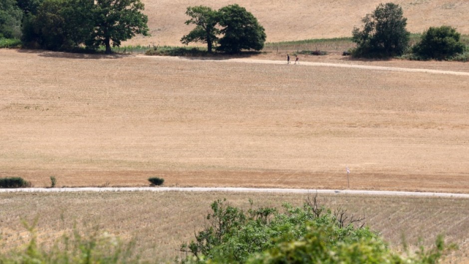 People walk on a dirt track between dry fields, turned brown from the heat of the sun near Guildford, southwest of London