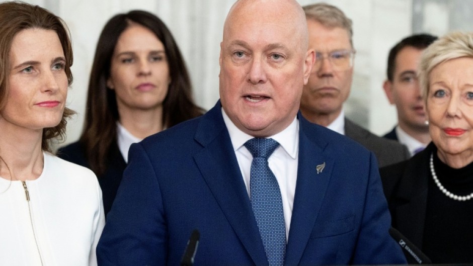 New Zealand Prime Minister Chris Luxon, flanked my his caucus, speaks to the media after surviving a second National party leadership vote at Parliament in Wellington on August 12, 2026