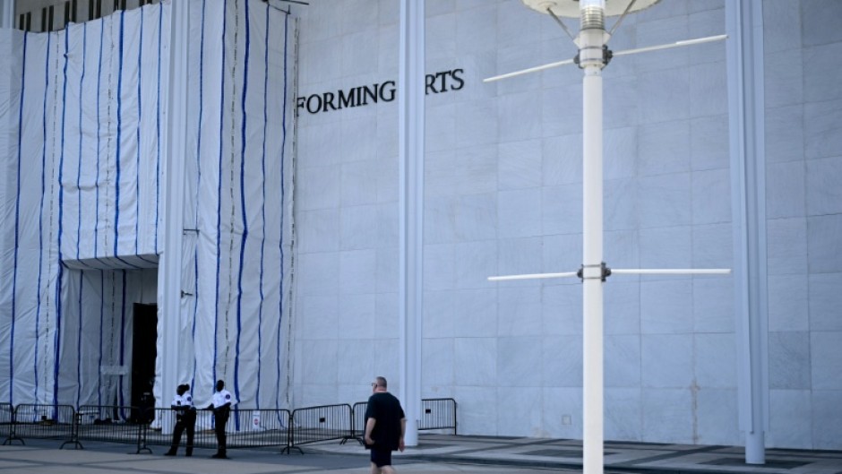 A person walks past scaffolding and a large protective tarp covering the facade of the John F. Kennedy Center for the Performing Arts