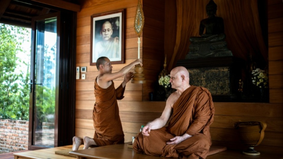 British and Thai Buddhist monk Shaun Chiverton, now known as Ajahn Jayasaro, sits as another monk holds a ceremonial fan in Bangkok