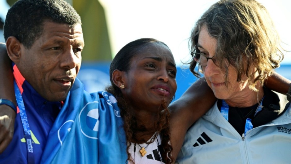 Ethiopia's Tigst Assefa (C) is helped off the track after crossing the finish line