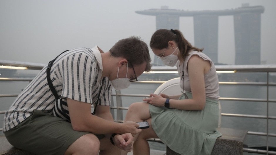 Tourists wear protective masks while seated across Marina Bay Sands in Singapore on October 15, 2026, as the country continues to be shrouded in haze caused by fires in Indonesia