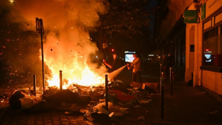 Residents use a fire extinguisher on burning trash near a metro station following a demonstration in central Paris