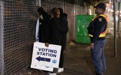 A SAPS officer looks on as an IEC officials take signs down after closing a polling station in Mowbray. AFP/Rodger Bosch